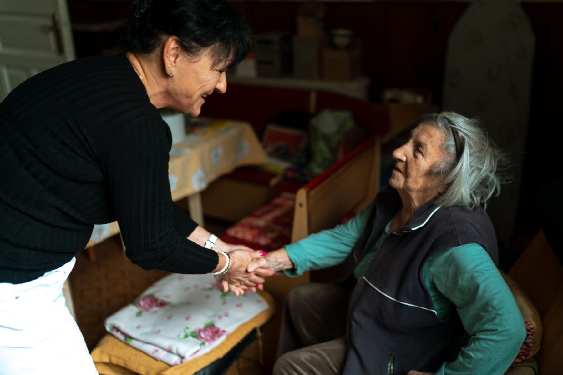 A caregiver holding an older adult’s hands during a conversation at home